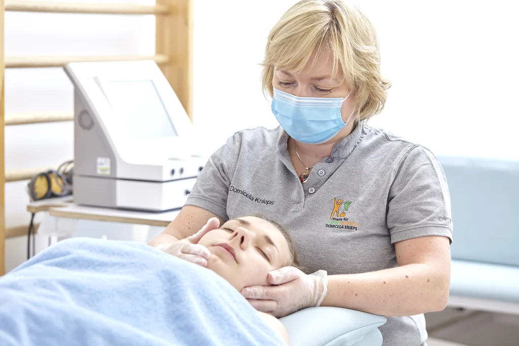 Die Therapeutin tastet den Kiefer einer Patientin von außen ab.