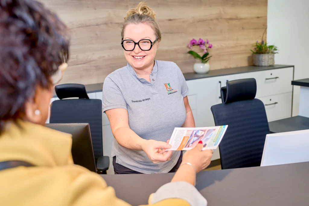Die Praxisinhaberin Domicela Knieps überreicht einer Patientin einen Flyer zu einem Präventionskurs.