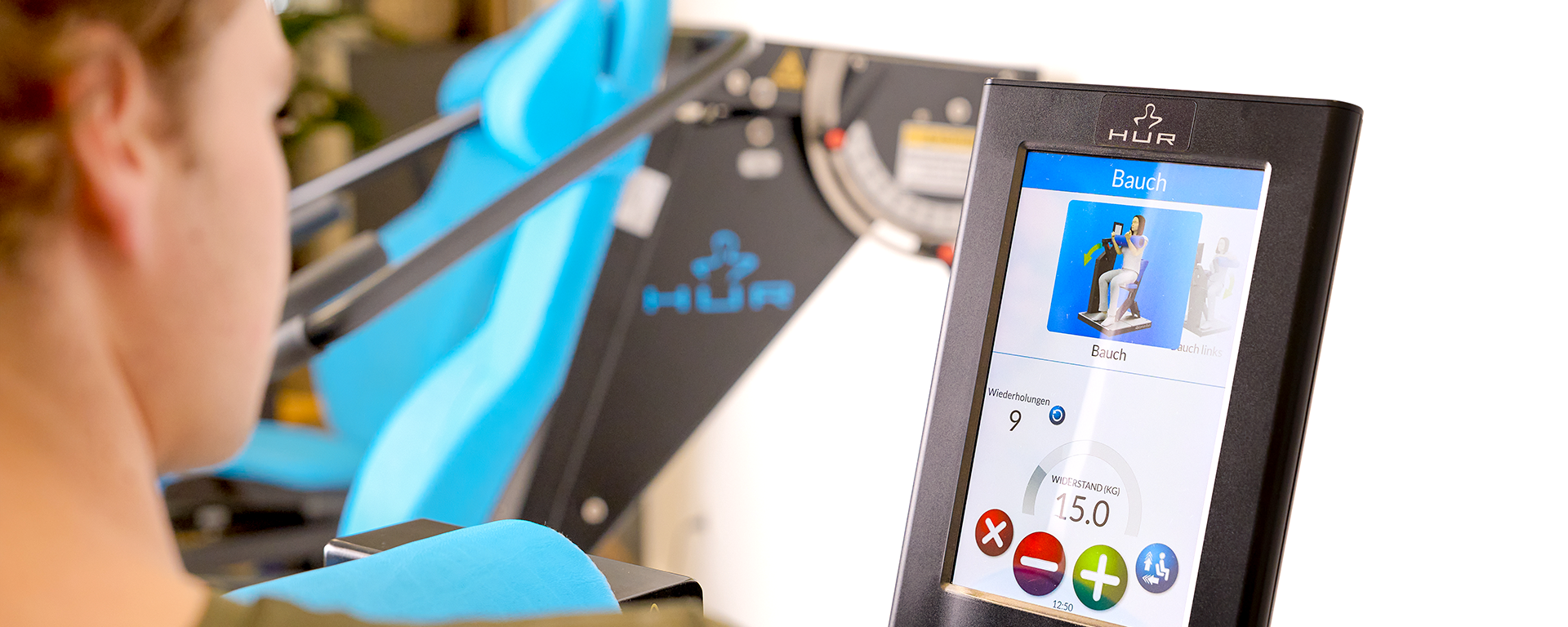 Ein junger Mann sitzt vor einer digitalen Anzeige, auf der ihm eine Trainingseinheit für die Bauchmuskulatur angezeigt wird.