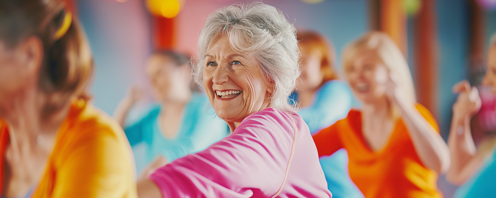 Eine Seniorin mit pinkfarbenem Shirt lacht herzhaft während Sie sich in einen Kreis von Menschen einreiht.